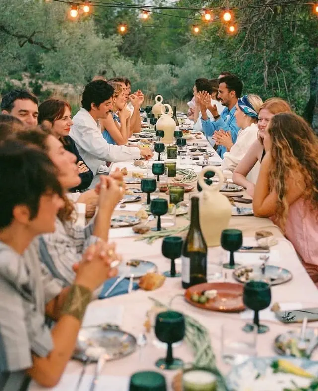 Grand dîner de groupe en terrasse au coucher du soleil, sous des guirlandes lumineuses
